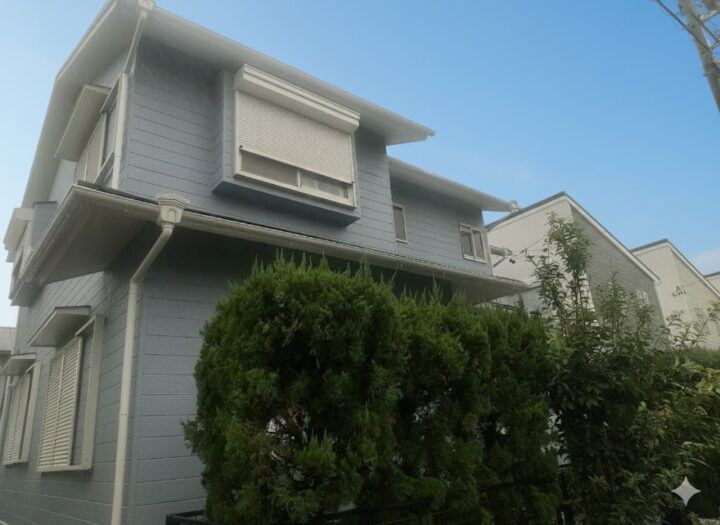 植栽の奥に見える、スモーキーブルーの外壁の戸建て住宅